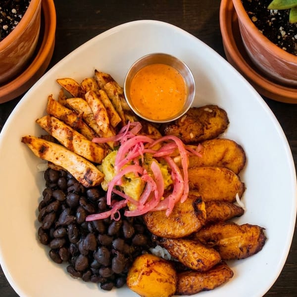 A white bowl filled with grilled chicken, black beans, fried plantains, and pickled red onions.