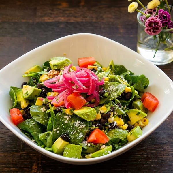 A vibrant salad with spinach, avocado, corn, black beans, tomatoes, and pickled red onions.