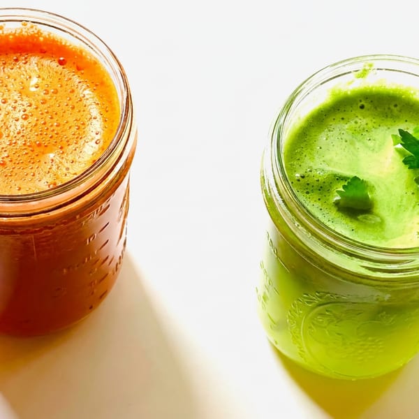 Two mason jars, one with orange juice and the other with green juice garnished with parsley.