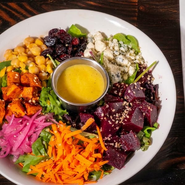A colorful salad with chickpeas, sweet potatoes, beets, and blue cheese, with dressing on a wooden table.