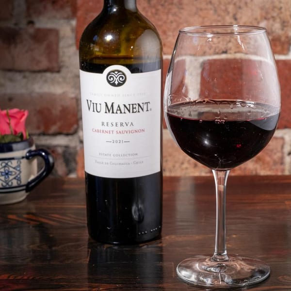 A bottle of Viu Manent Reserva Cabernet Sauvignon wine next to a full glass of red wine.